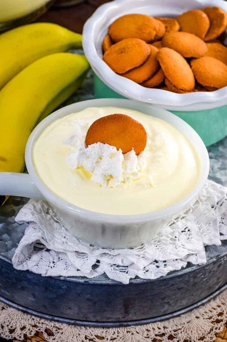 a small white bowl filled with this easy banana pudding recipe topped with whipped cream and a vanilla wafer 