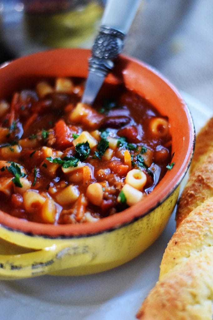 an overhead view of this pasta fagioli soup recipe inside of a stoneware bowl with handles and crispy bread