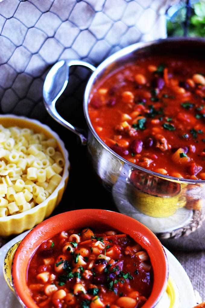 an overhead view of this stovetop pasta fagioli soup recipe with a serving bowl of the soup and a separate bowl with the cooked pasta noodles 