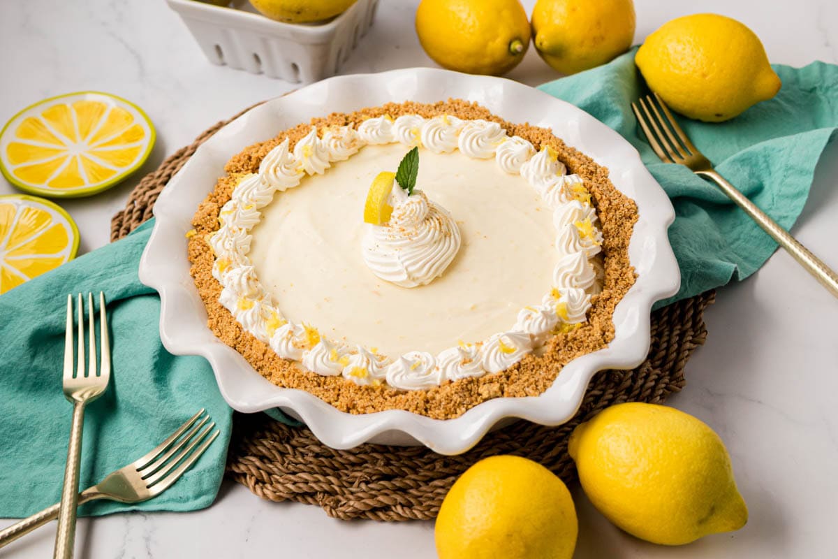 A whole no bake lemon Icebox pie in a white pie plate garnish with whipped cream, a lemon wedge, and mint leaves.