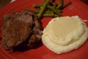 a red plate with garlic roast beef, green beans, and creamy whipped potatoes