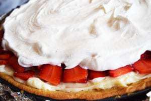 A closeup of this strawberry pizza topped with whipped cream on a sugar cookie crust