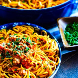 A bowl of Creamy Spicy Sausage Spaghetti Pasta garnished with fresh, chopped parsley in a big blue serving bowl