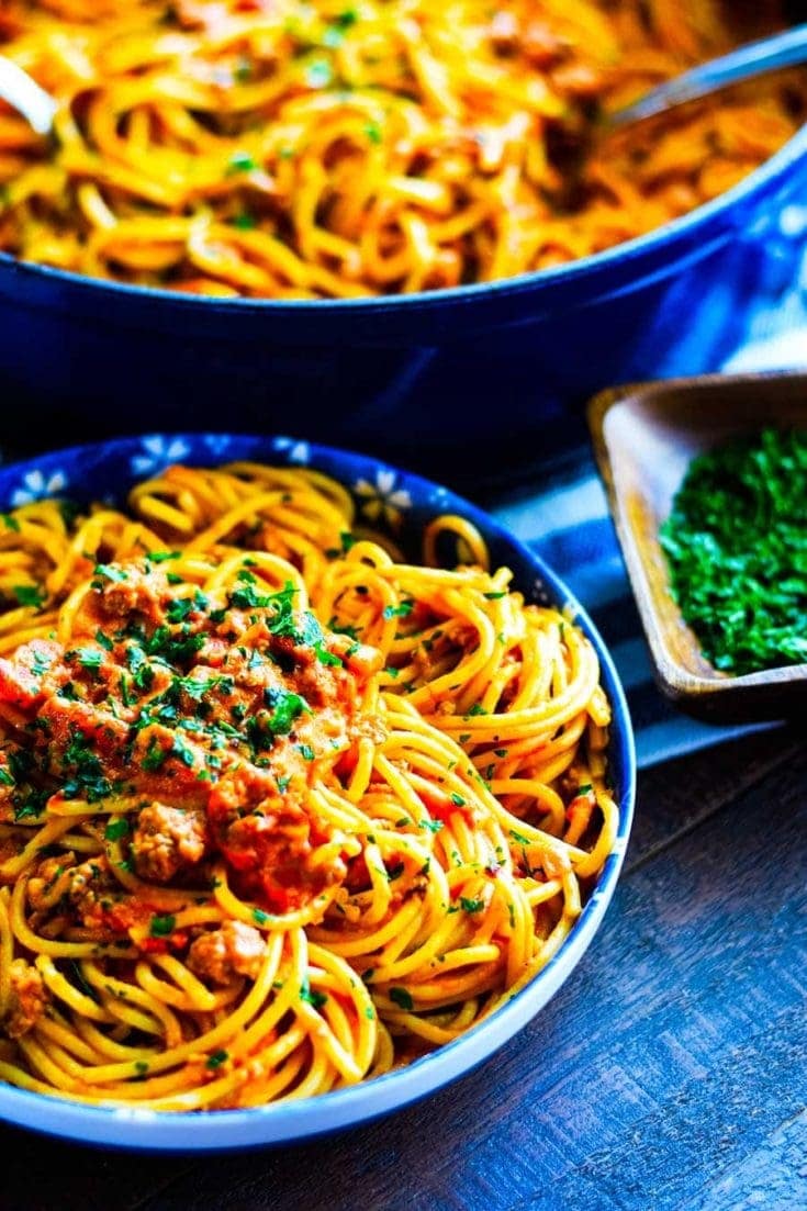 Sausage Spaghetti with a creamy tomato sauce in blue bowl with white flowers. Set on a wooden table and garnished with parsley.