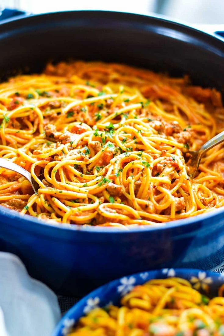 Creamy Spicy Spaghetti with Sausage topped with parsley in a blue casserole skillet being served with tongs.