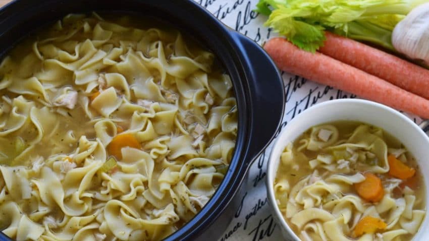 stovetop chicken noodle soup in a large Dutch oven and a white serving bowl