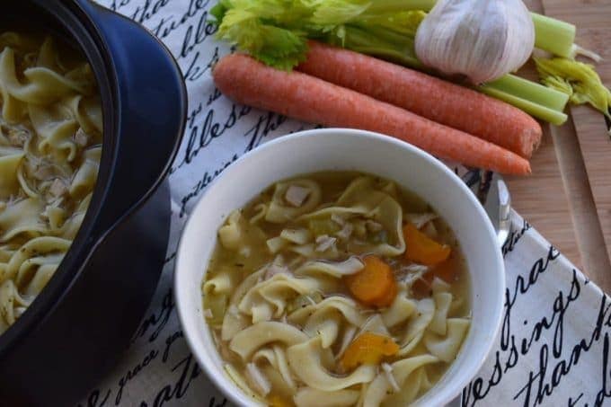 a white bowl filled with this easy chicken noodle soup recipe with carrots and celery in the background