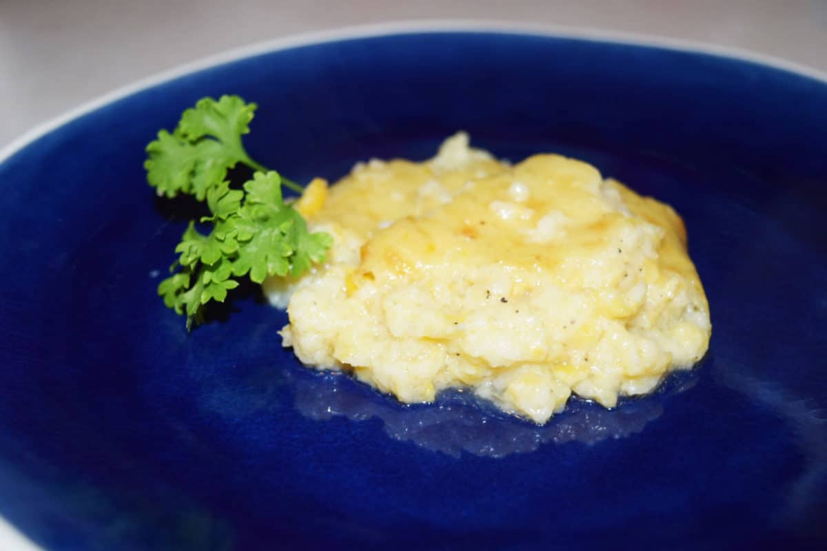 a serving of this corn casserole garnished with fresh parsley on a dark blue plate