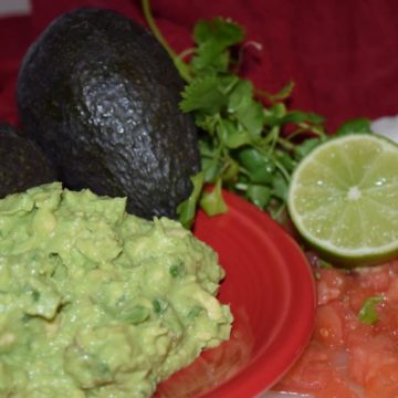 homemade guacamole on a red plate with cilantro, an avocado, and a lime in the background