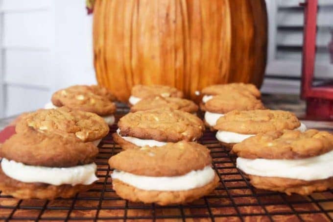 several pumpkin spice sandwich cookies aka pumpkin spice whoopie pies on a white cooking rack with an orange pumpkin in the background