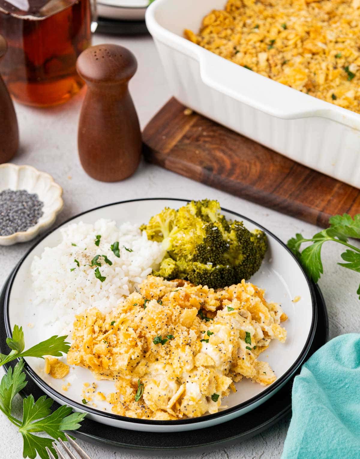 Poppy seed chicken casserole on a plate with white rice and broccoli with the casserole dish behind in the background.