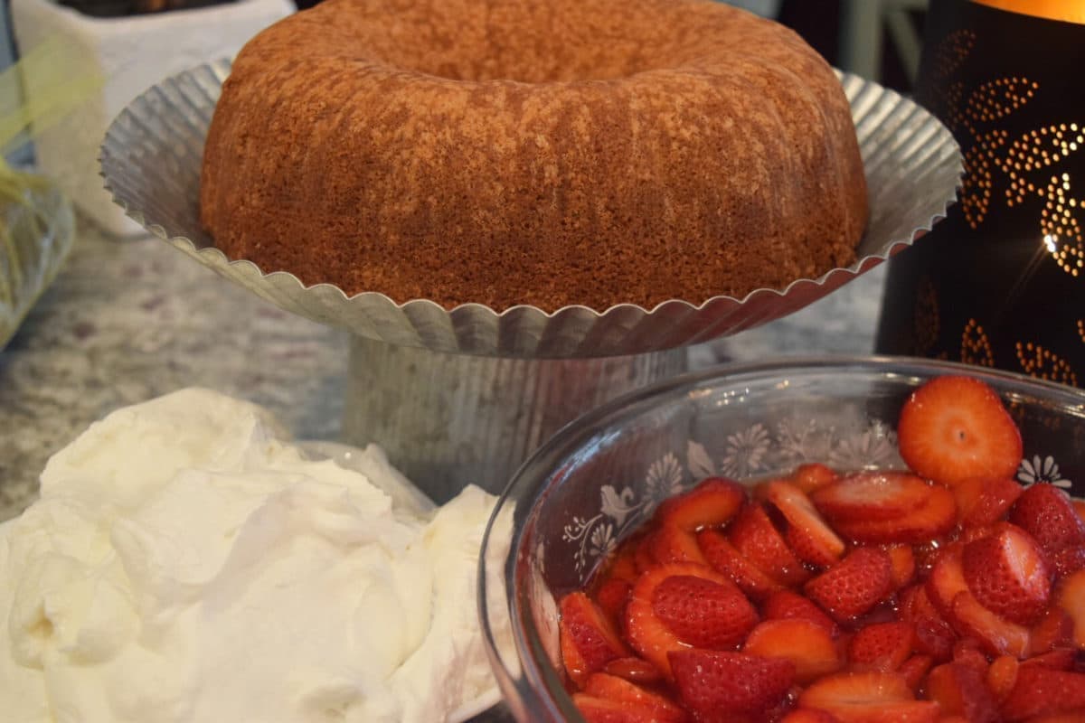 this homemade sour cream pound cake on a cake stand with amaretto soaked strawberries and fresh whipped cream