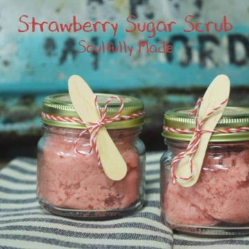 two glass jars of homemade strawberry sugar scrub with wooden spoons