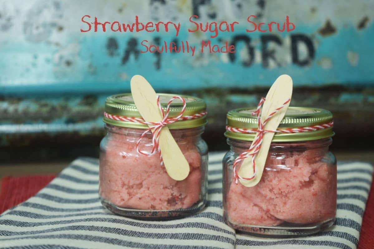 two glass jars of homemade strawberry sugar scrub with wooden spoons