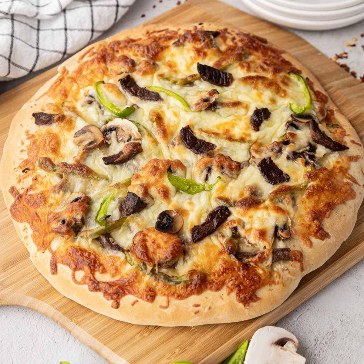 A Philly cheesesteak pizza on a wooden board.