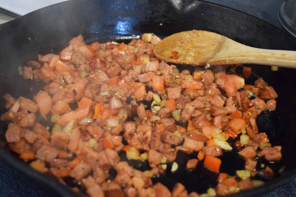 chopped andouille sausage browning in a a black cast iron skillet with a wooden spoon 