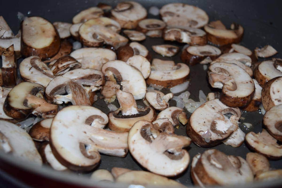 a black cast iron skillet filled with sliced baby portobello mushrooms to be used in the mushroom sauce for these fontina pork chops