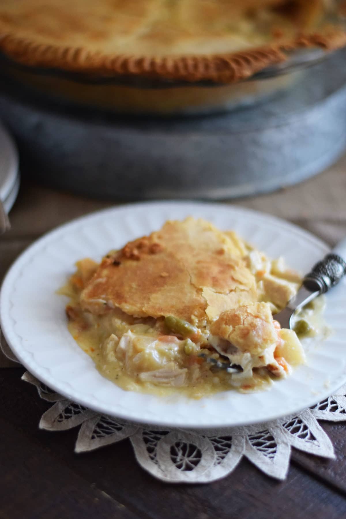 a side view of a slice of chicken pot pie from this easy chicken pot pie recipe on a white plate with a fork removing one bite\'s worth of the pie
