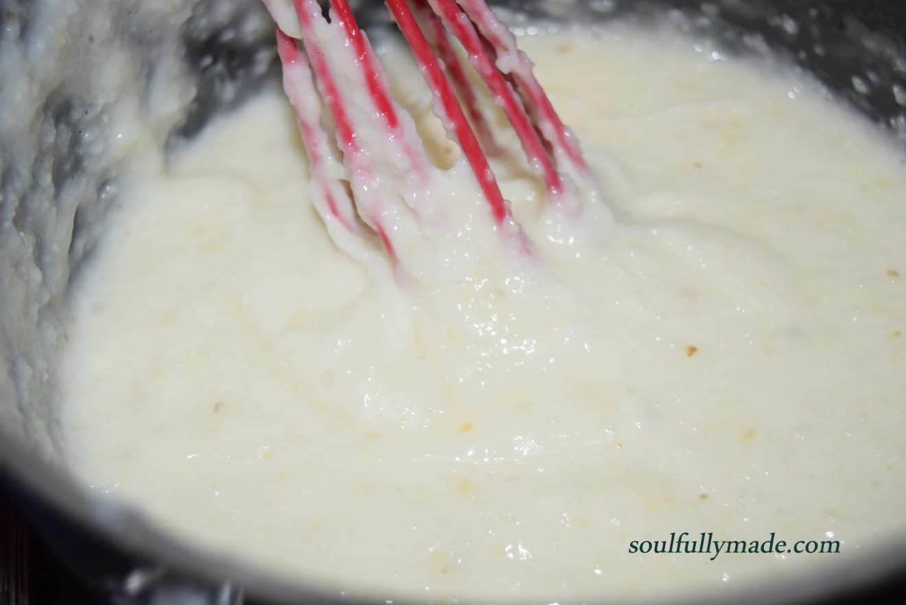 creamy white grits cooking in a saucepan with a red whisk 