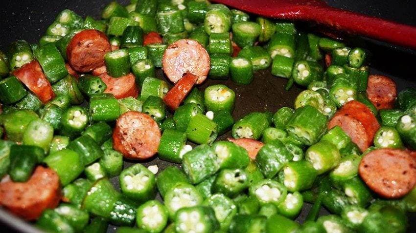 bright green chopped okra and slices of sausage browning in a skillet