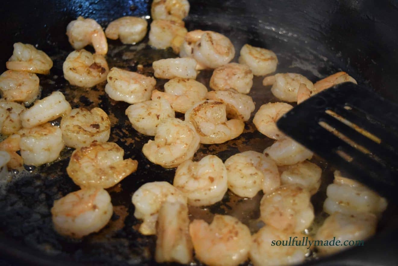 juicy pink shrimp sautéing in a black cast iron skillet for this shrimp and grits with andouille cream sauce recipe