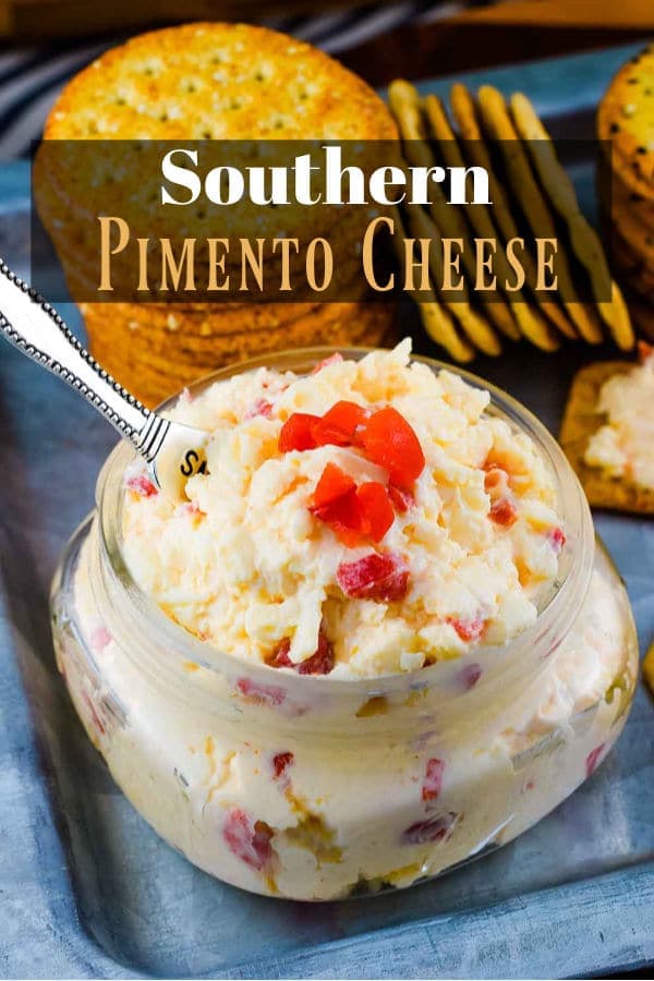 The Pinterest image for this Southern Pimento Cheese recipe in a glass jar with a serving spoon and topped with chopped pimento peppers