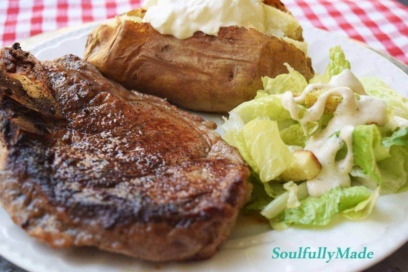a closeup of a ribeye steak, baked potato, and side salad on a plate for this steakhouse dinner at home recipe