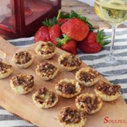 sweet dijon pecan baked brie bites on a wooden cutting board with fresh strawberries and a glass of champagne in the background