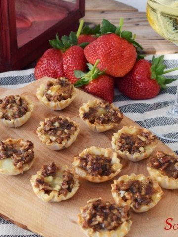 sweet dijon pecan baked brie bites on a wooden cutting board with fresh strawberries and a glass of champagne in the background