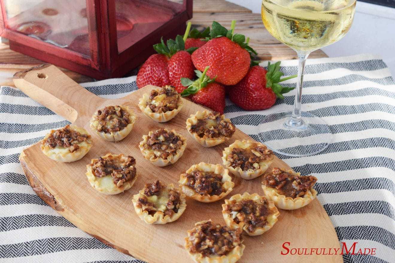 sweet dijon pecan baked brie bites on a wooden cutting board with fresh strawberries and a glass of champagne in the background