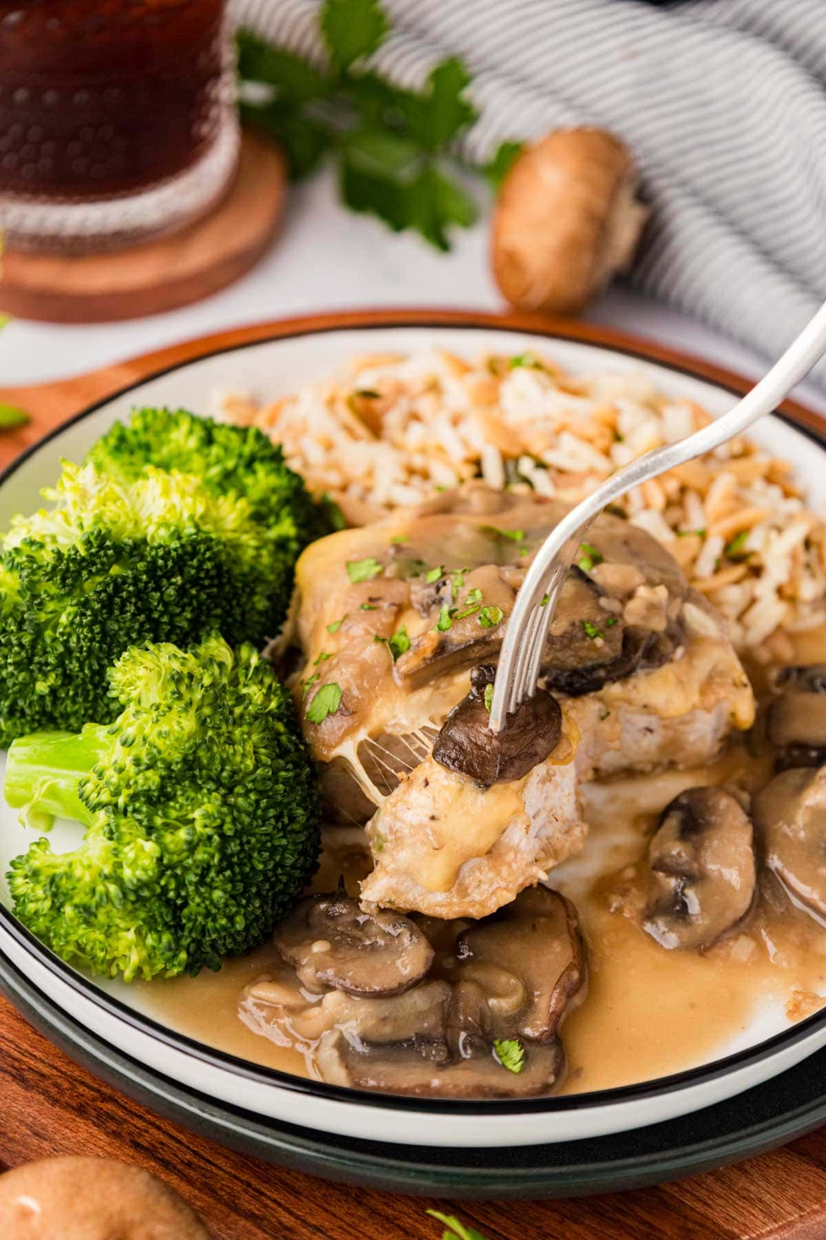 A fork removing a bike of pork chop and marsala mushroom sauce.