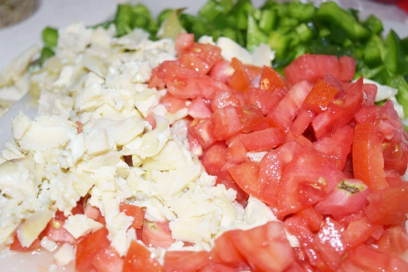 Chopped tomatoes, green pepper, and artichokes in a bowl.