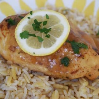 a closeup of this instant pot lemon and garlic glazed chicken recipe served over rice with a lemon slice and chopped parsley