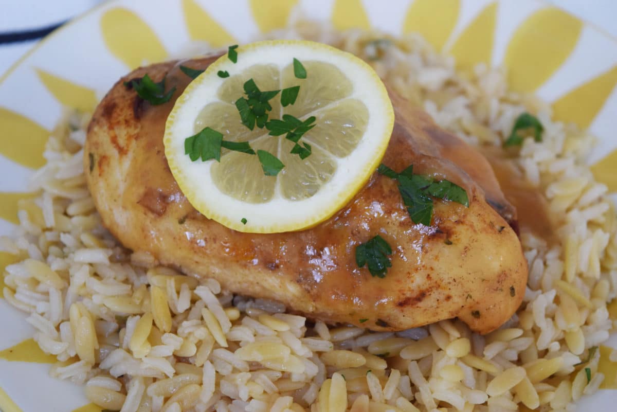 a closeup of this instant pot lemon and garlic glazed chicken recipe served over rice with a lemon slice and chopped parsley