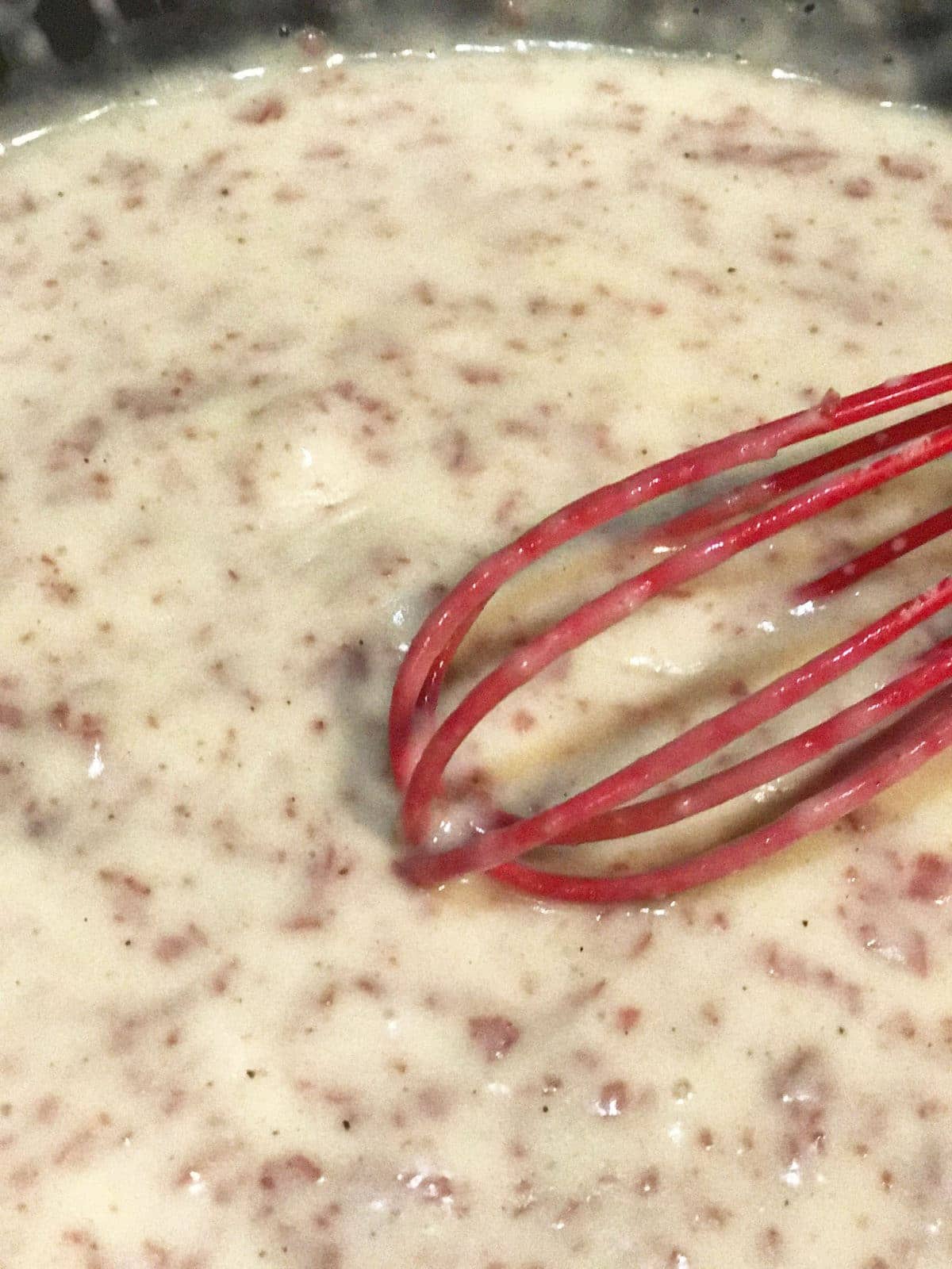 chipped beef gravy with a red whisk in a pan
