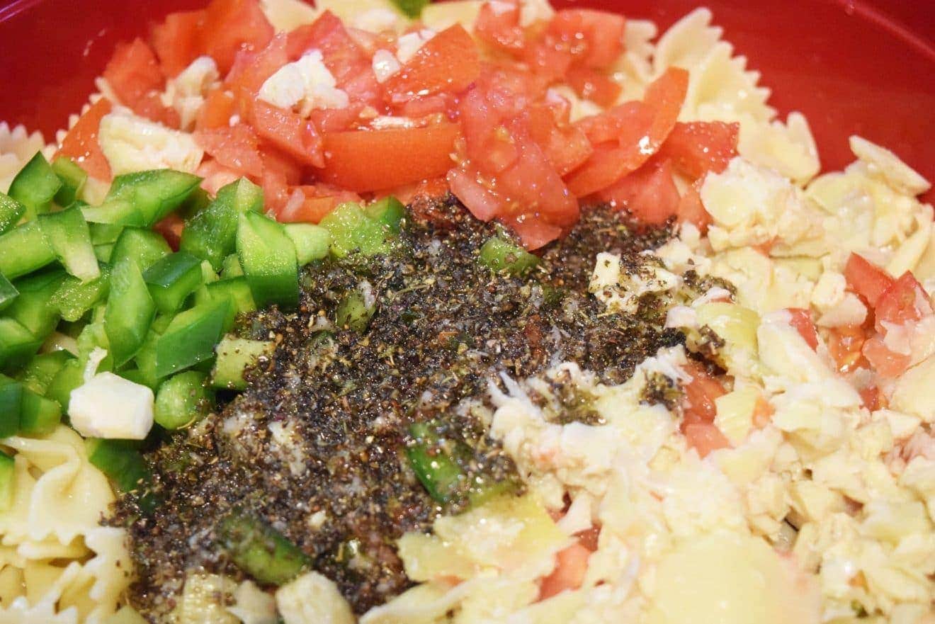 A close-up of a plate of food with chopped tomatoes, green pepper, and artichokes along with vinaigrette in a bowl.