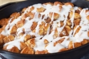 a black cast iron skillet filled with these apple pie biscuit bites topped with a sweet glaze
