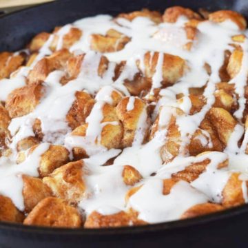 a black cast iron skillet filled with these apple pie biscuit bites topped with a sweet glaze