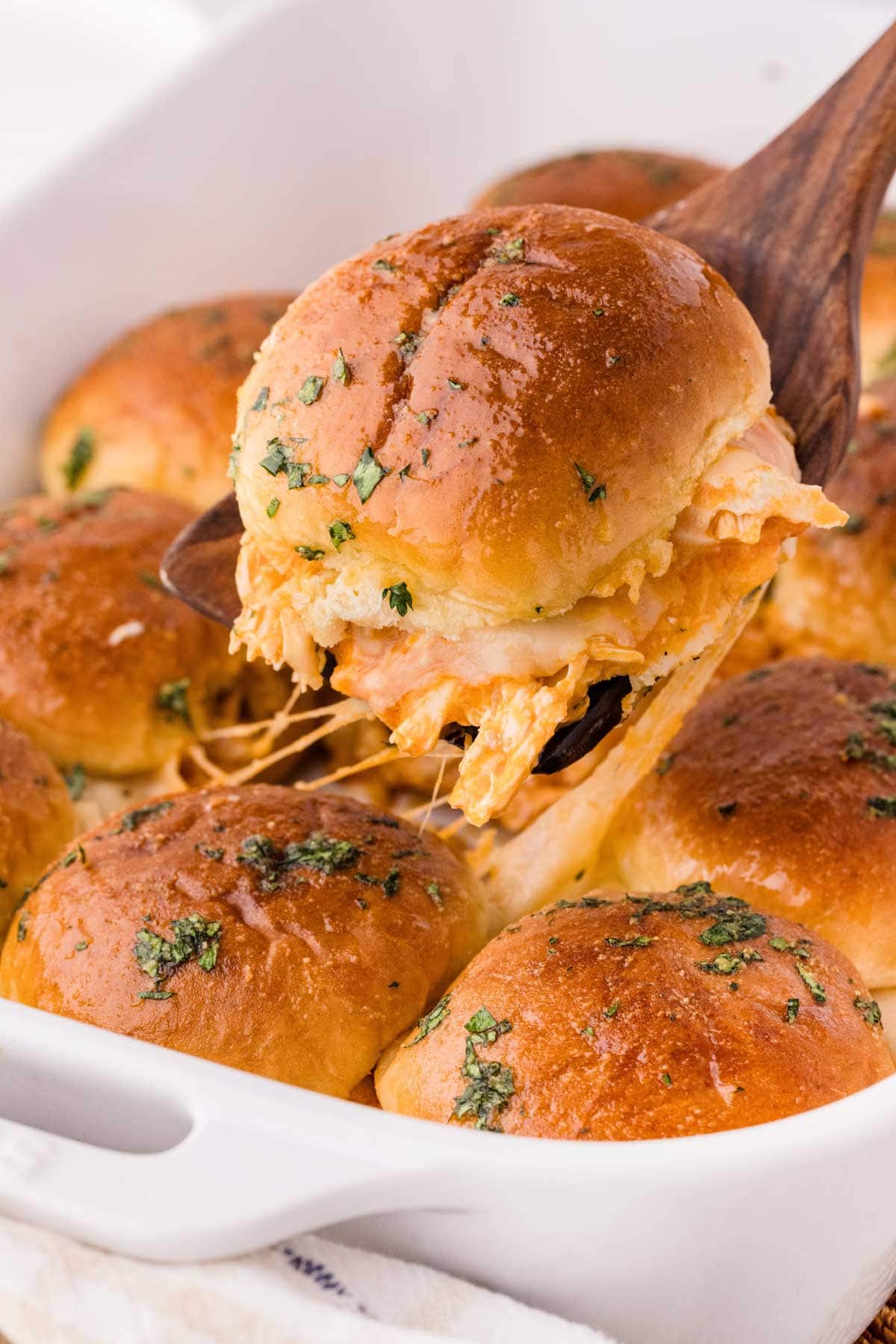 A wooden spatula removing a buffalo chicken slider from the baking dish.