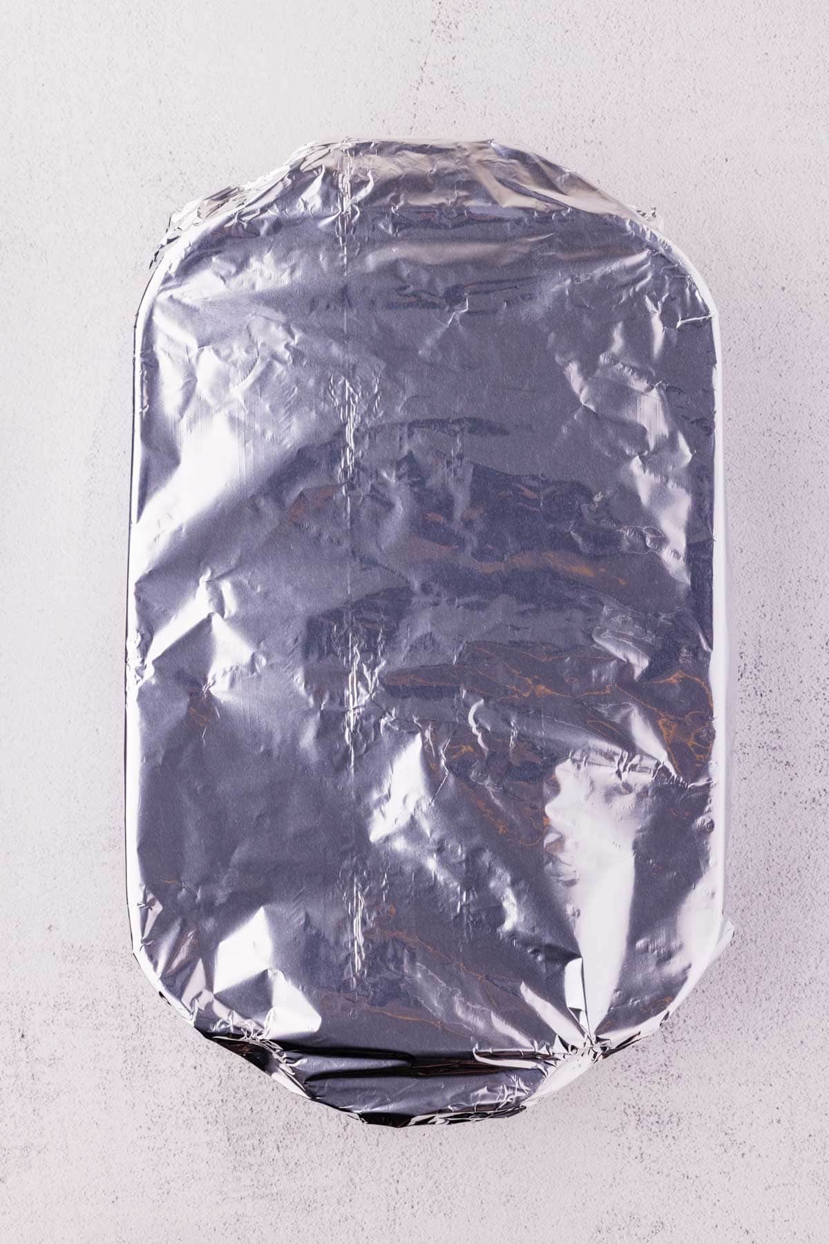 Foil covering buffalo sliders in a baking dish.