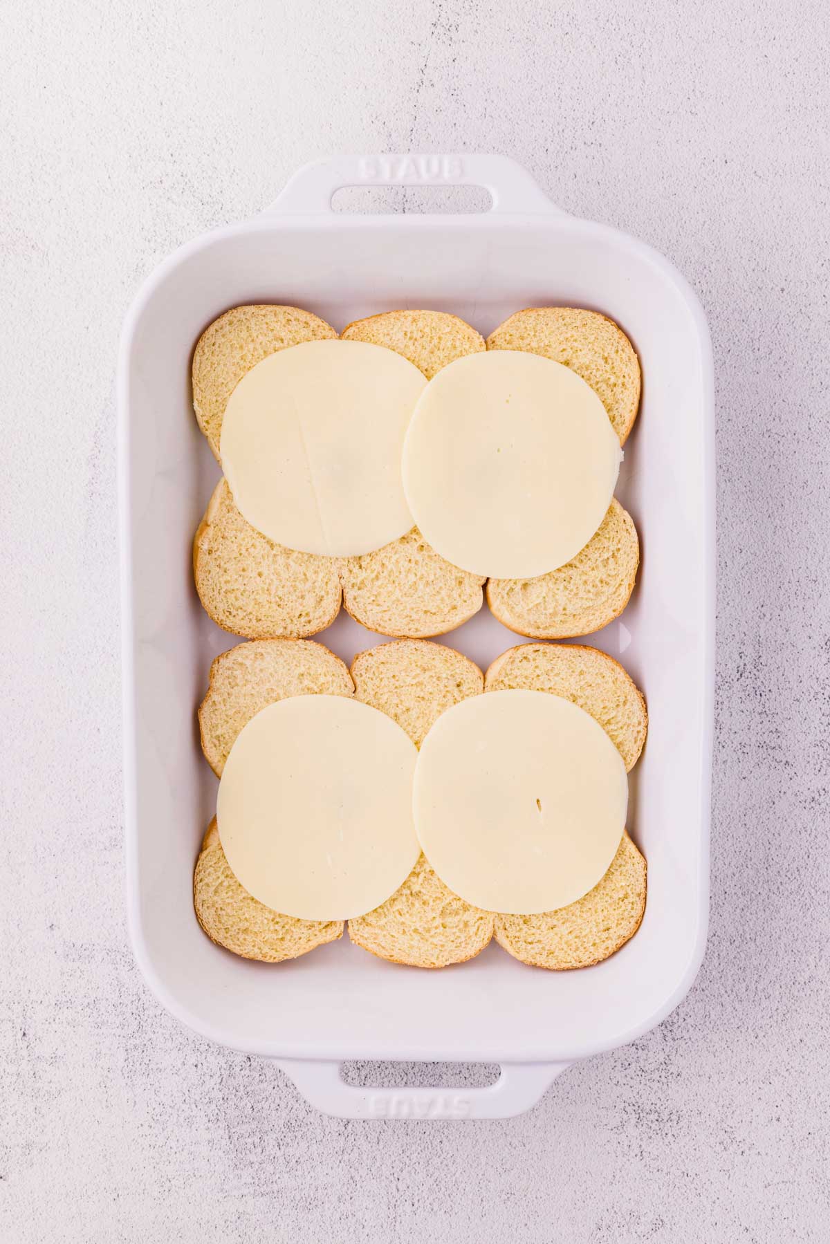 Bottom half of slider buns topped with cheese in a 9 X 13 pan.