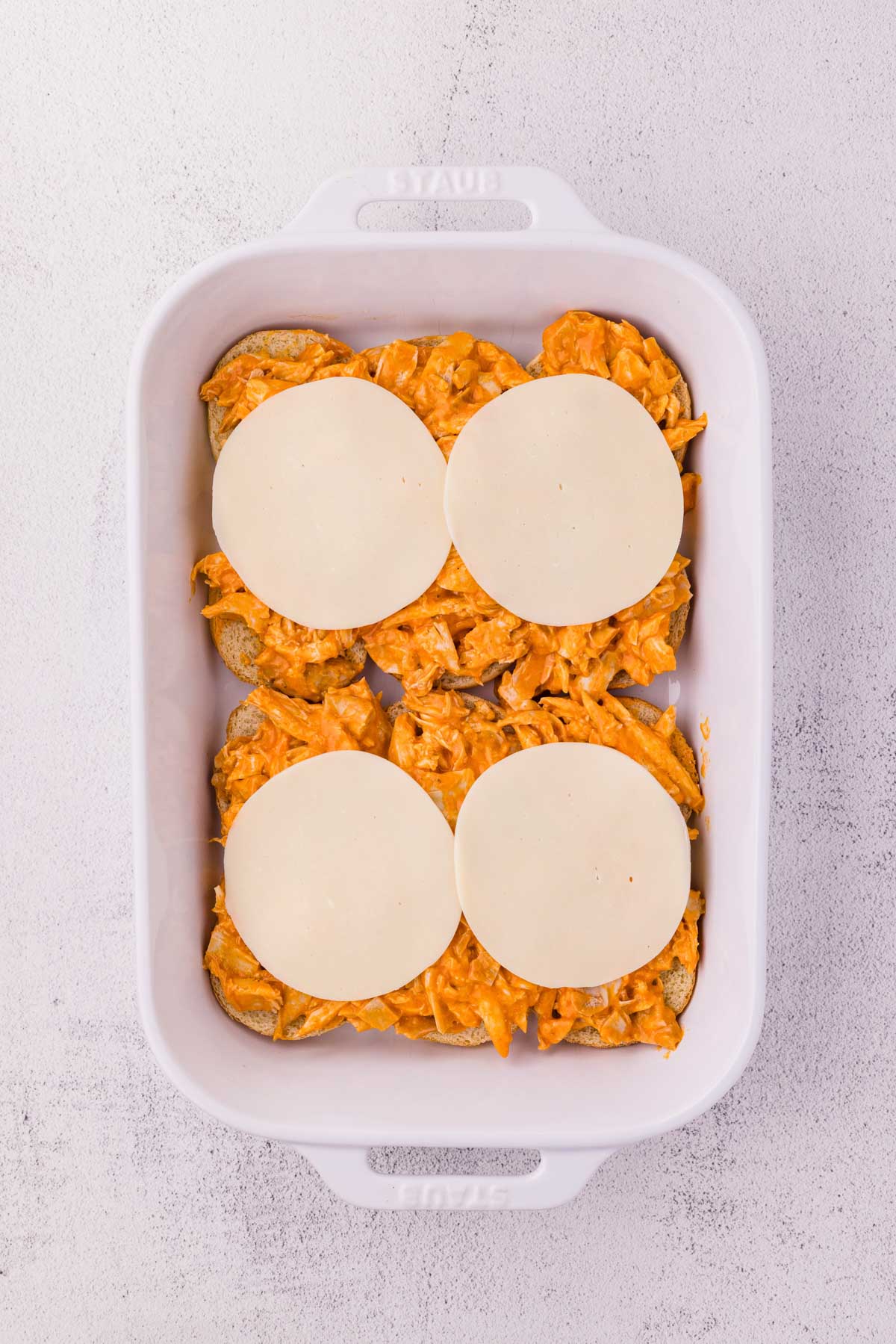 Cheese slices added to buffalo chicken on sliders.