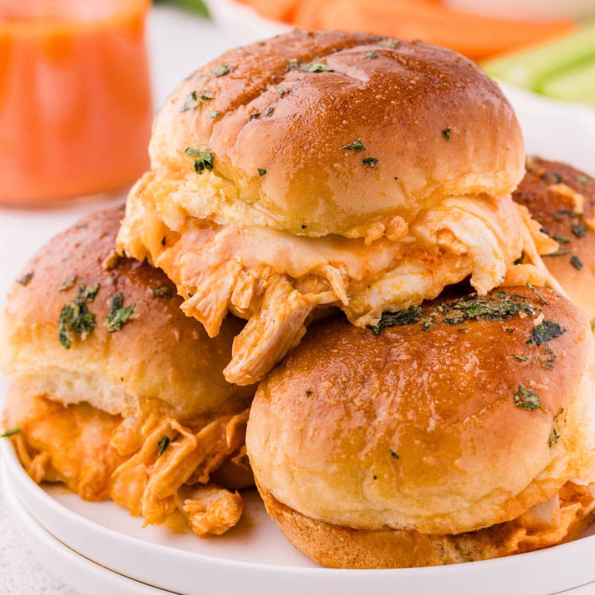 A white plate stacked with buffalo chicken sliders.