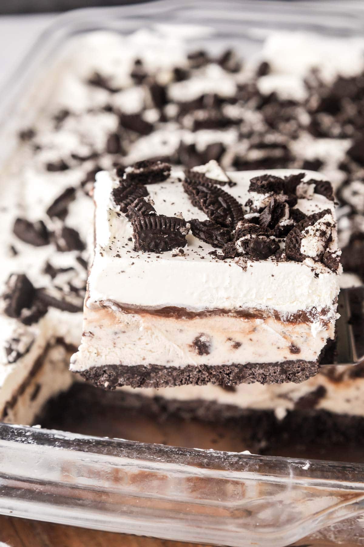 A slice of Oreo, ice cream cake being removed from a glass pan.