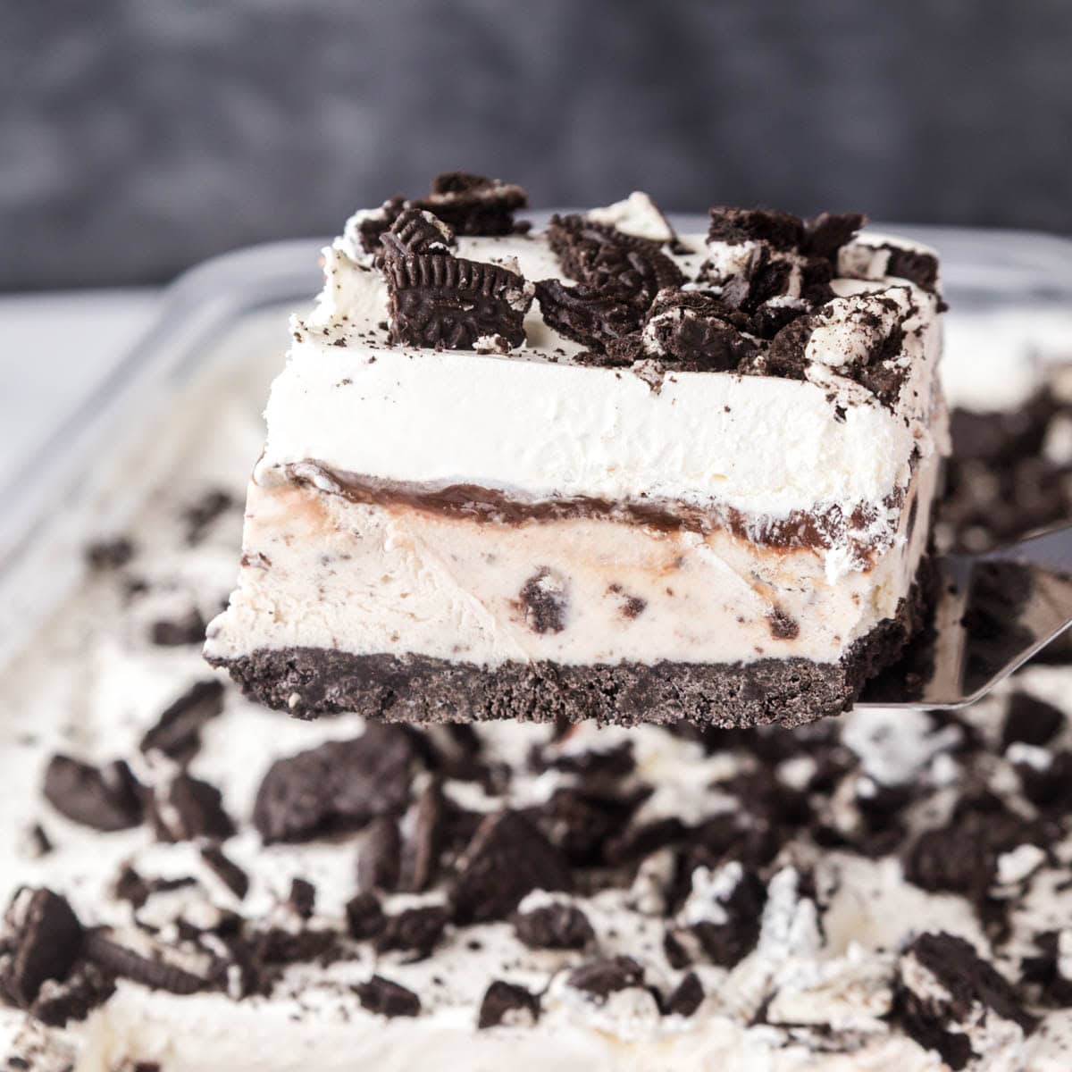 A slice of Oreo, ice cream cake being removed from a glass pan.