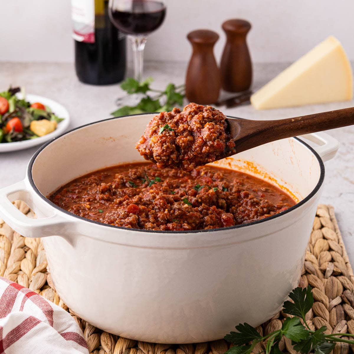 Homemade meat sauce in a white dutch oven with a wooden spoon removing a scoop.