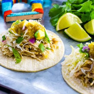 an overhead view of two salsa verde chicken street tacos with lime wedges in the background