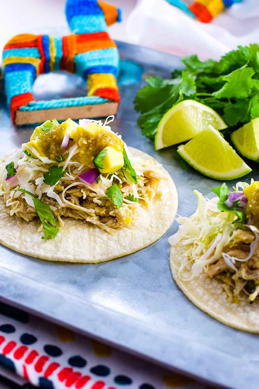 an overhead view of two salsa verde chicken street tacos with lime wedges in the background 