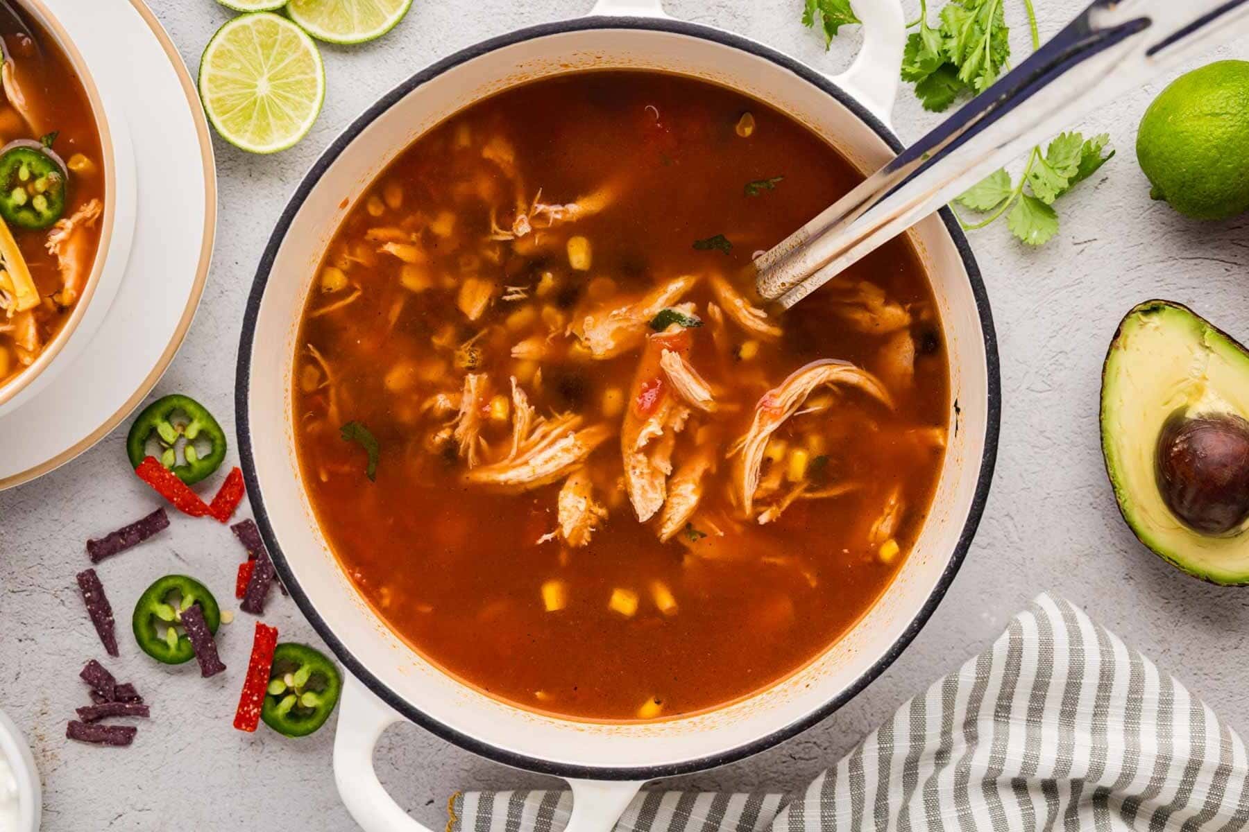 A white dutch oven filled with chicken tortilla soup and a ladle removing a spoon full.