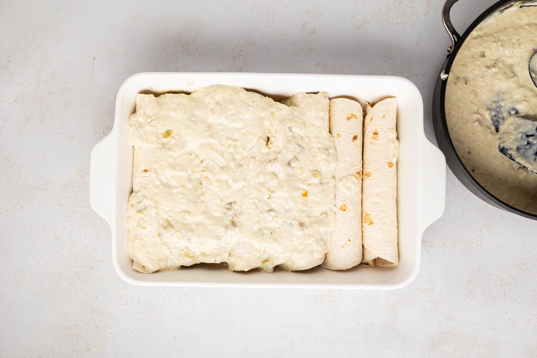 Enchiladas in the casserole dish with green chile sauce on top.